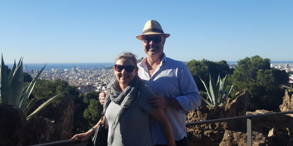 Mell and her partner standing together at a scenic lookout in Barcelona, overlooking the city and coastline, reflecting on choosing a different path and defining success on their own terms.